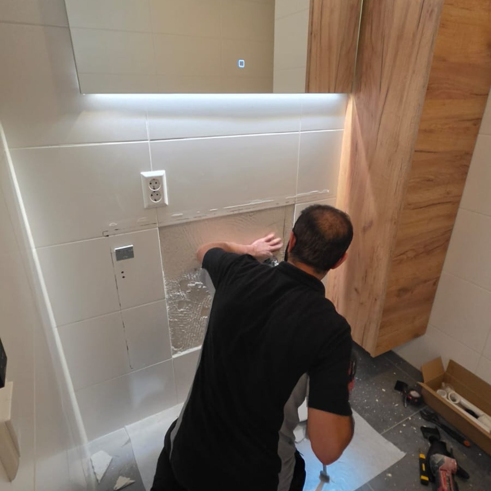 Badkamer afmonteren | Nour Klusbedrijf Vakman werkt aan de wand onder een verlichte badkamerspiegel