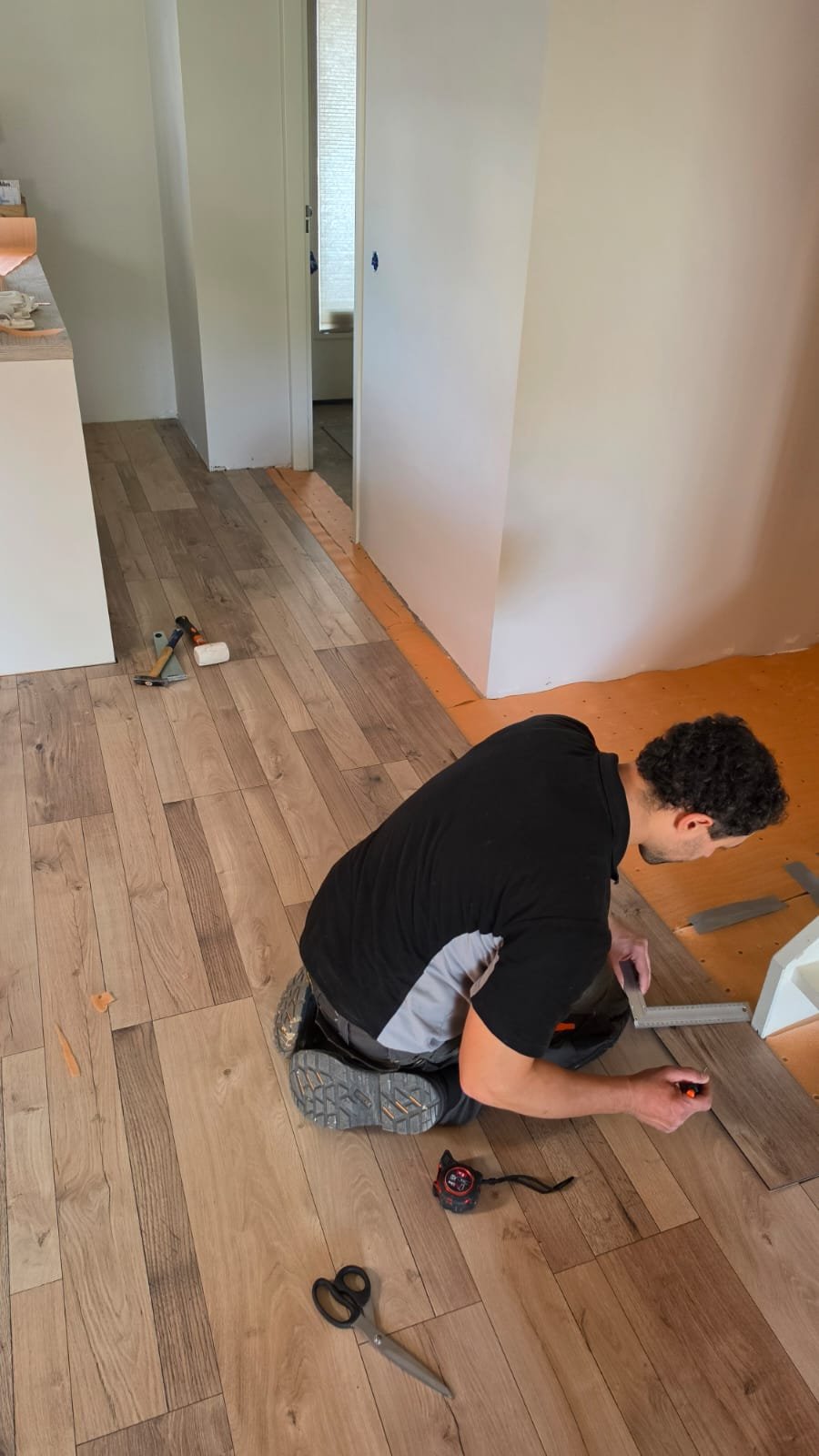 PVC-vloer leggen in de woonkamer | Nour Klusbedrijf Vakman meet een PVC-vloerplank op maat tijdens het leggen van een houtlook vloer